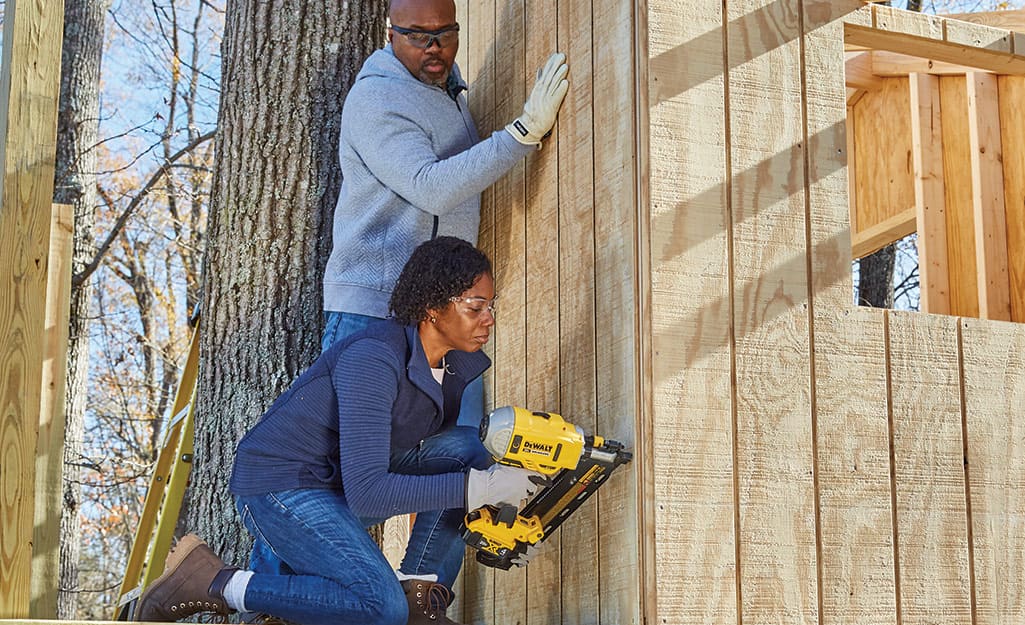 Couple attaches siding to a treehouse frame. Couple attaches siding to a treehouse frame.