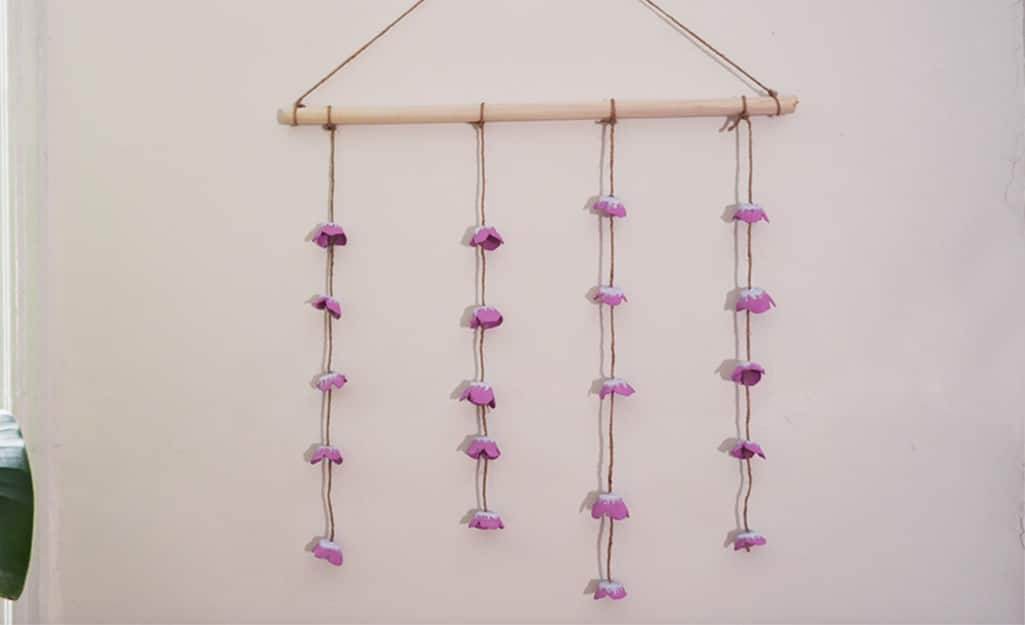 Flowers made from an egg carton hang from twine on a wall. 