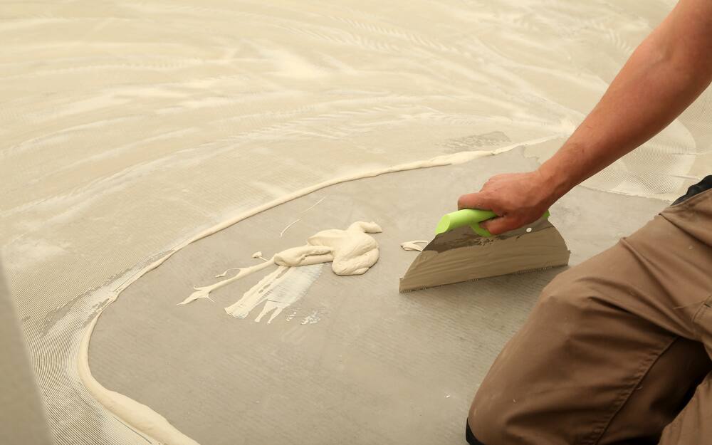 Man uses trowel to spread vinyl adhesive on concrete floor. Man uses trowel to spread vinyl adhesive on concrete floor.