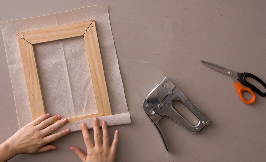A cut drop cloth is being measured to a frame. A cut drop cloth is being measured to a frame.