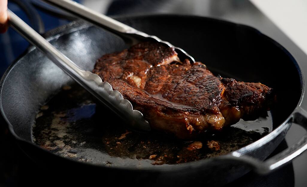 A steak is being seared in a cast iron frying pan. A steak is being seared in a cast iron frying pan.