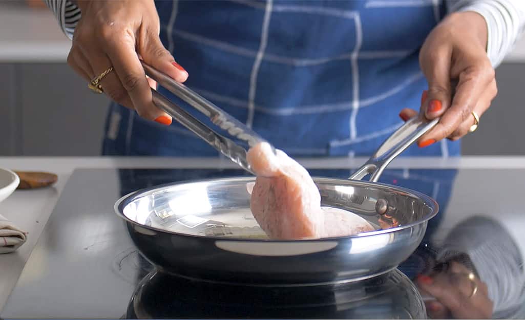 A woman cooks chicken in a Stainless steel pan. A woman cooks chicken in a Stainless steel pan.
