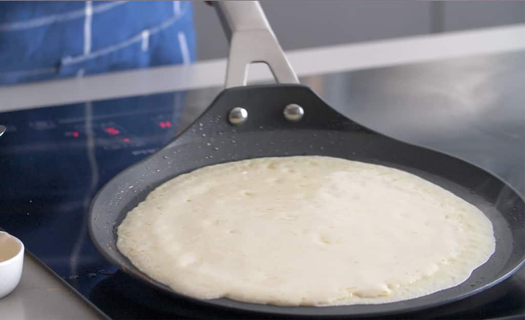 A crepe pan is used to cook a pancake. A crepe pan is used to cook a pancake.