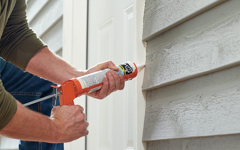 A man caulking the exterior of a new entry door. A man caulking the exterior of a new entry door.