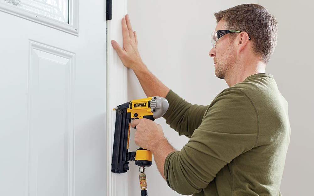 A man nailing trim on a new entry door. A man nailing trim on a new entry door.