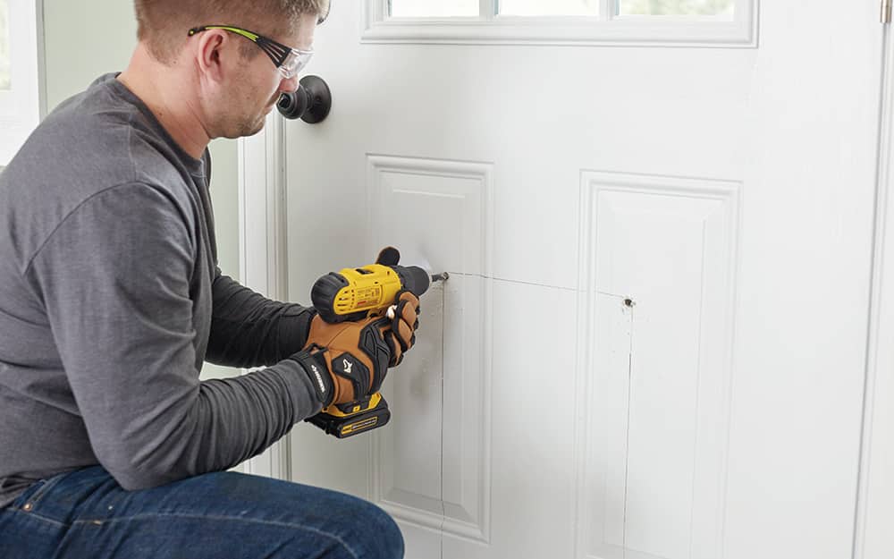 A man drilling holes into the bottom of an exterior door A man drilling holes into the bottom of an exterior door