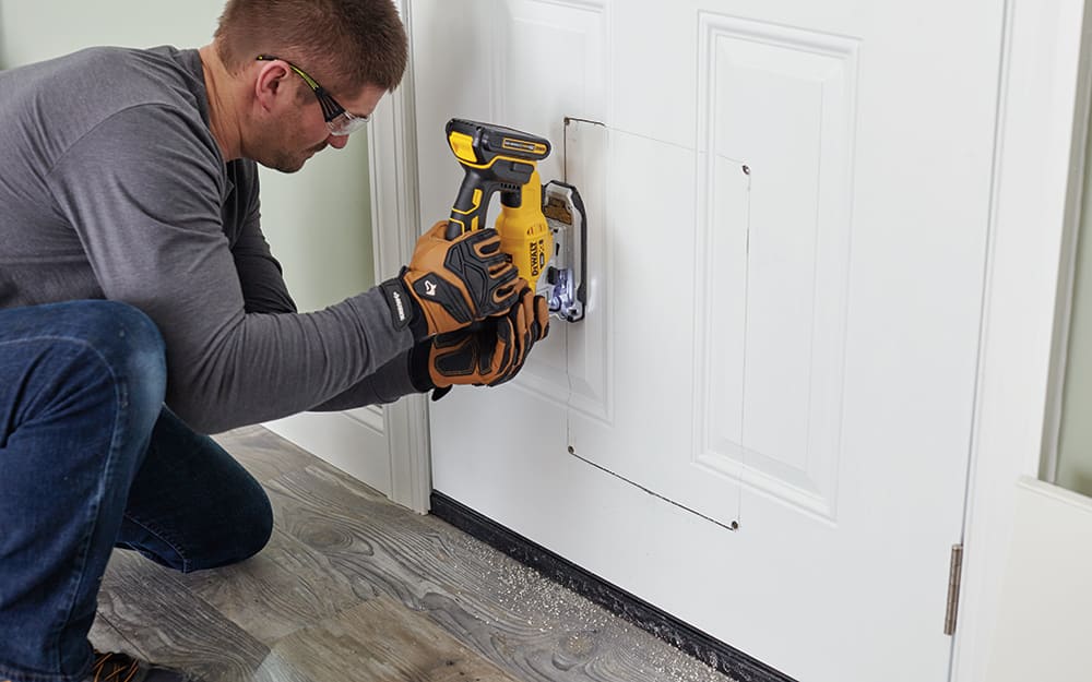 A man cutting into the bottom of an exterior door A man cutting into the bottom of an exterior door
