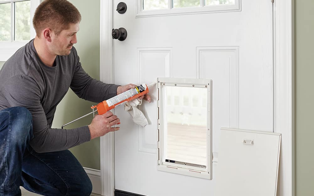 A man sealing the frame of a dog door into an exterior door A man sealing the frame of a dog door into an exterior door