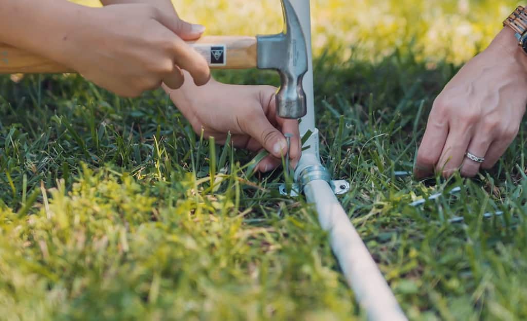 A person anchoring a DIY kids sprinkler to a lawn with a U-bolt. A person anchoring a DIY kids sprinkler to a lawn with a U-bolt.