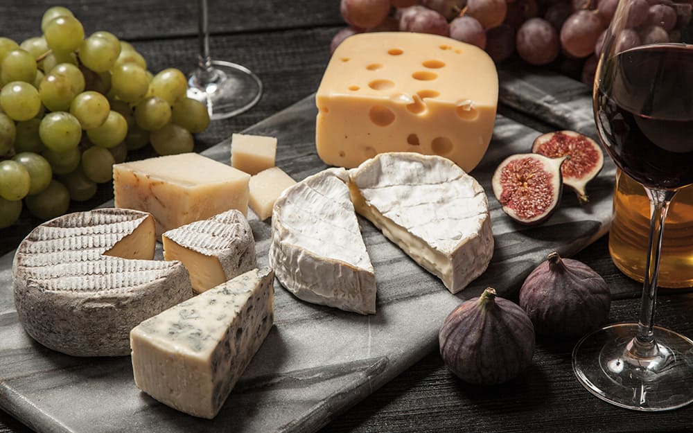 A marble cutting board with assorted cheeses and fruits arranged on top. A marble cutting board with assorted cheeses and fruits arranged on top.