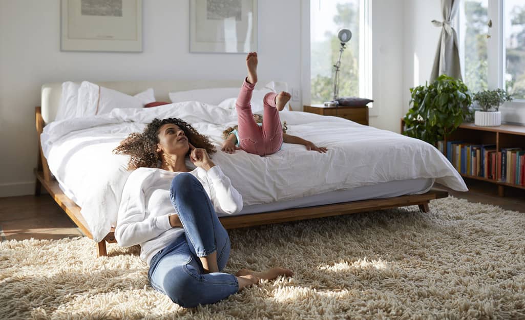 Someone sitting on a floor beside a bed. Someone sitting on a floor beside a bed.