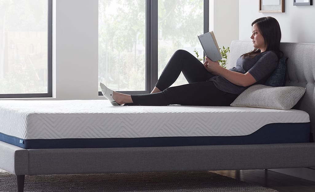 A woman reading on a bed with an uncovered memory foam mattress. A woman reading on a bed with an uncovered memory foam mattress.
