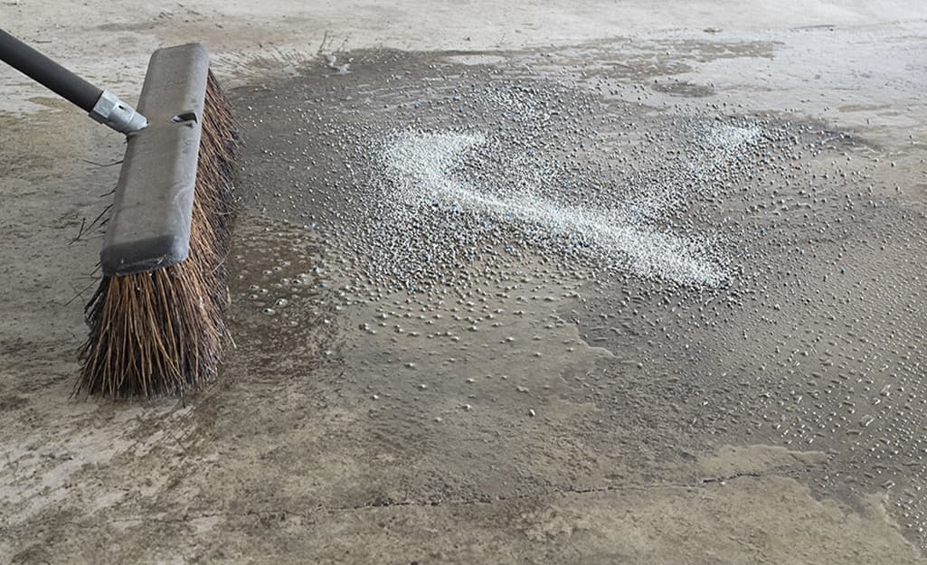 A person sweeps a concrete floor with a push broom. A person sweeps a concrete floor with a push broom.
