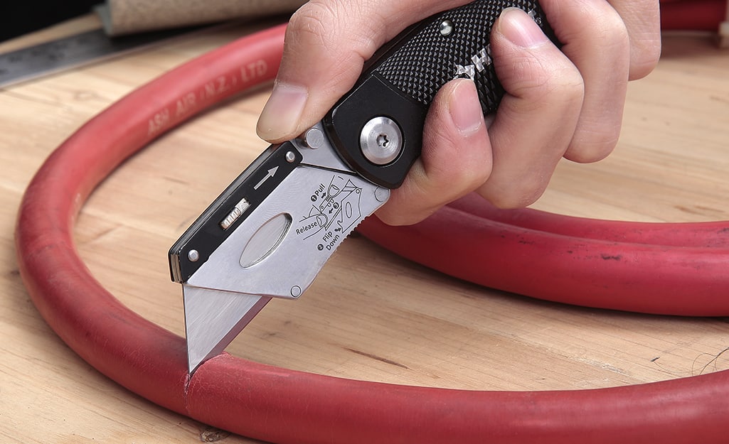 A person cuts a hose with a utility knife. A person cuts a hose with a utility knife.