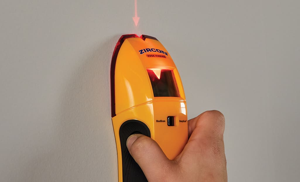 A person uses a stud finder on a wall. A person uses a stud finder on a wall.