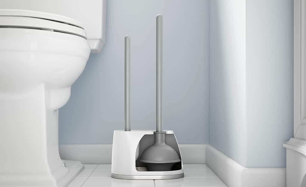 A plunger sits next to a toilet in a bathroom. A plunger sits next to a toilet in a bathroom.