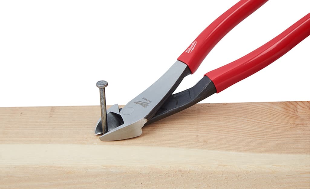 A set of pliers pulls a nail from a piece of wood. A set of pliers pulls a nail from a piece of wood.