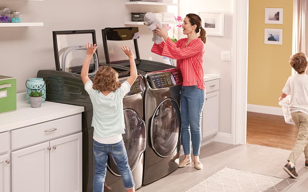 A child helps his mother add clothes to a washer and dryer in a laundry room. A child helps his mother add clothes to a washer and dryer in a laundry room.