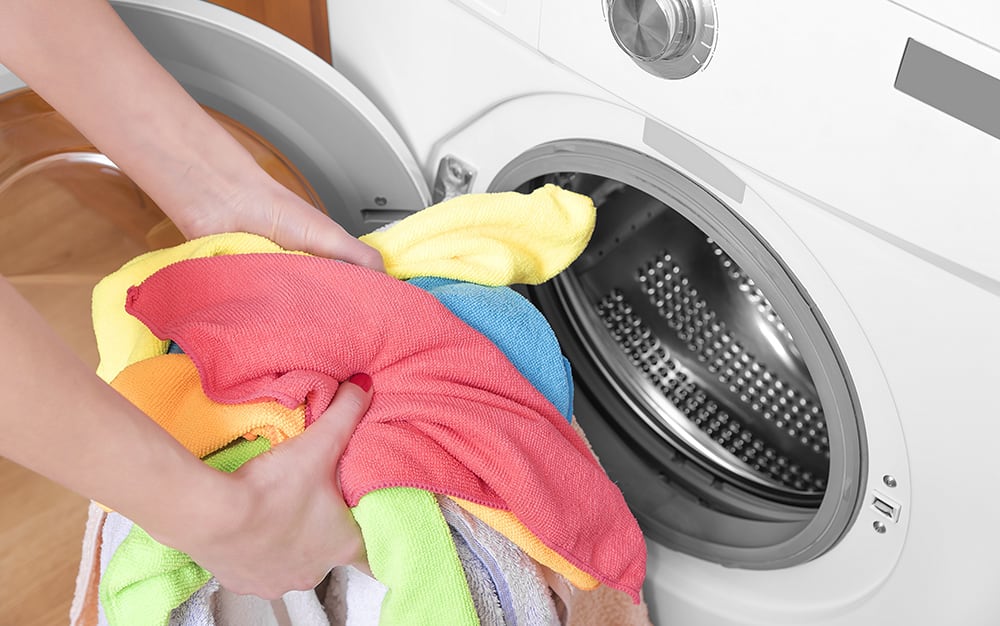 A person holds a handful of colorful laundry in front of a dryer. A person holds a handful of colorful laundry in front of a dryer.