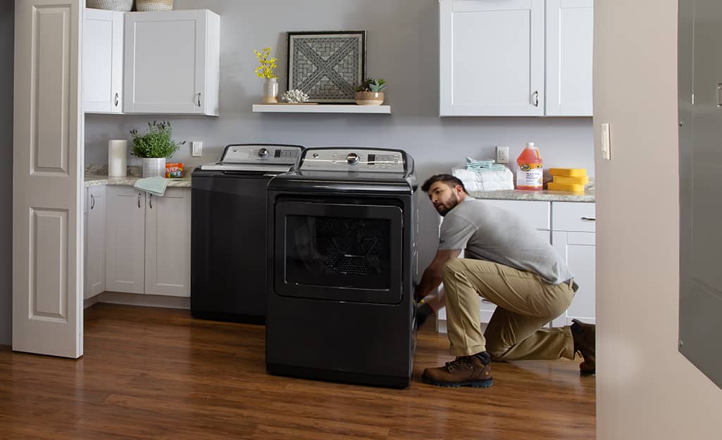 A man kneels down to install a new washing machine and dryer in a laundry room. A man kneels down to install a new washing machine and dryer in a laundry room.