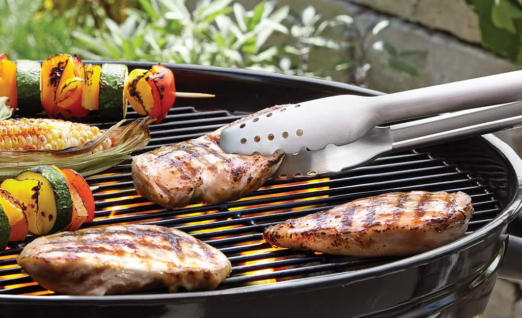 A person uses tongs to flip their grilled chicken. A person uses tongs to flip their grilled chicken.