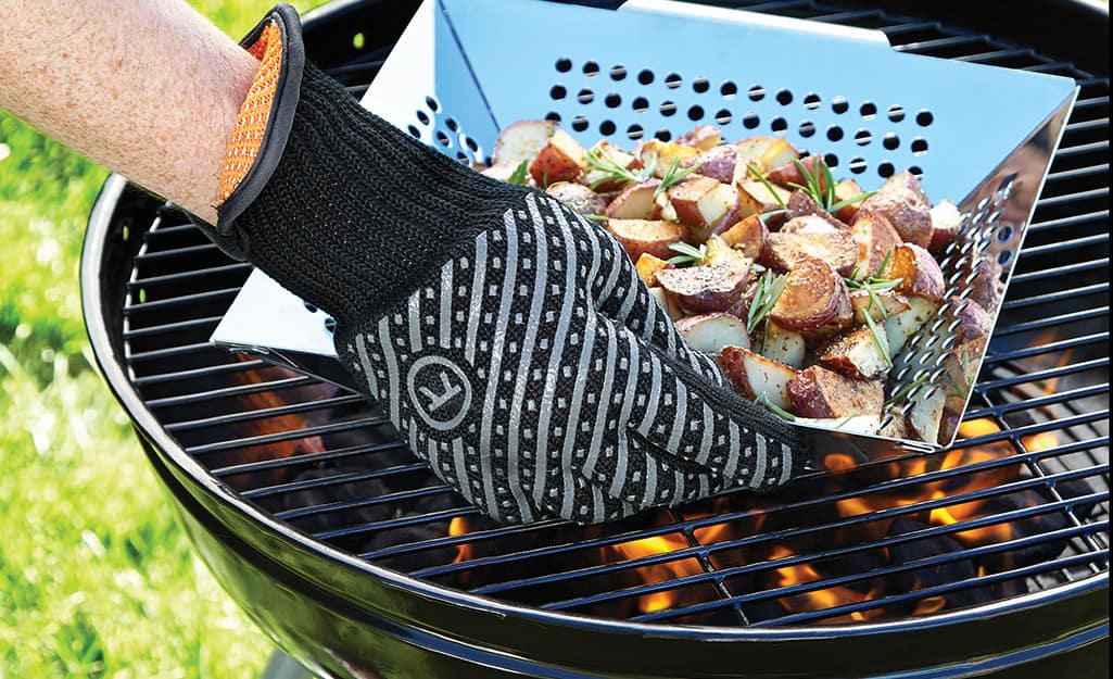 A person wears grilling gloves when using a charcoal grill. A person wears grilling gloves when using a charcoal grill.