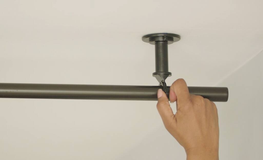 A person hangs a curtain rod on a ceiling-mounted hook. A person hangs a curtain rod on a ceiling-mounted hook.
