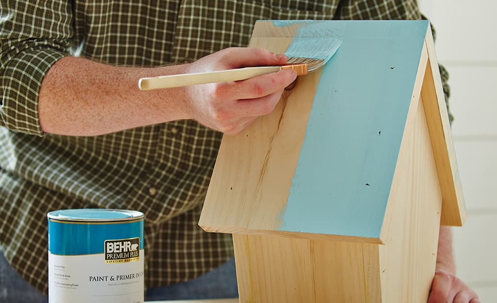 A person paints the roof of a birdhouse a light blue A person paints the roof of a birdhouse a light blue