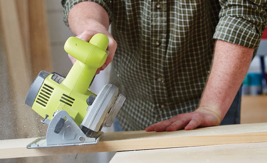 A person cuts a board with a circular saw while building a birdhouse. A person cuts a board with a circular saw while building a birdhouse.