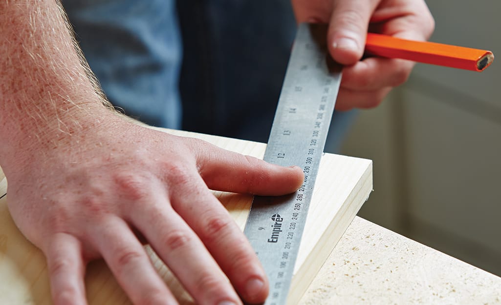 A person uses a pencil and a ruler to mark a cut line on a piece of wood needed to build a birdhouse A person uses a pencil and a ruler to mark a cut line on a piece of wood needed to build a birdhouse