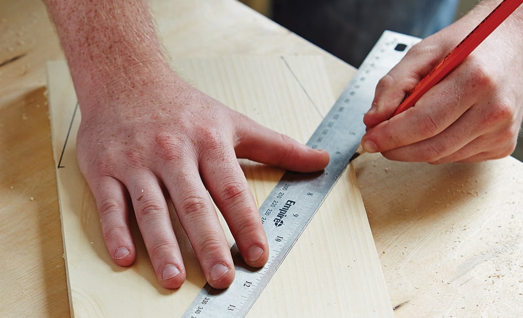 A person uses a pencil and a ruler to mark the bottom cut lines for a DIY birdhouse A person uses a pencil and a ruler to mark the bottom cut lines for a DIY birdhouse
