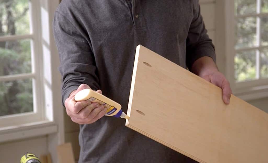 A man squeezing wood glue onto the edge of a board. A man squeezing wood glue onto the edge of a board.