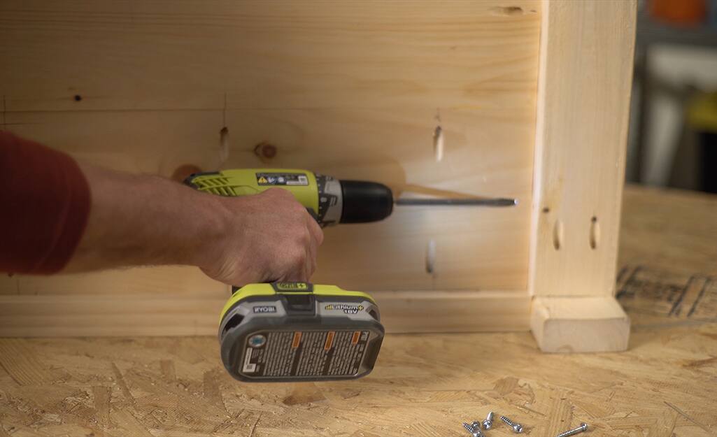 A man using a drill to make pocket holes in a DIY coffee table. A man using a drill to make pocket holes in a DIY coffee table.
