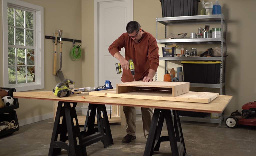 A man using a drill to screw together a shelf for a DIY coffee table. A man using a drill to screw together a shelf for a DIY coffee table.