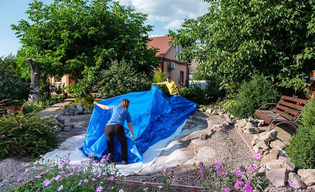 Two people laying a pond liner as they build an in-ground fish pond. Two people laying a pond liner as they build an in-ground fish pond.