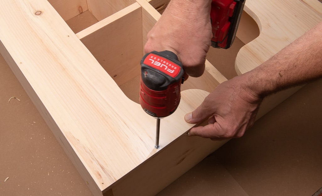 A person drilling screws into the backing of the cubby storage. A person drilling screws into the backing of the cubby storage.