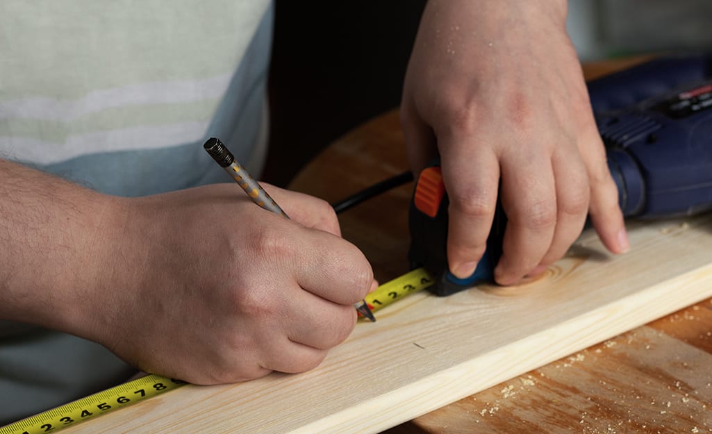 A person measuring a board with a tape measure. A person measuring a board with a tape measure.
