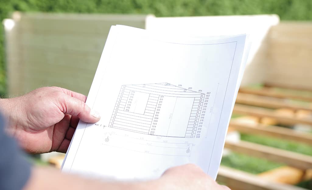 A person holds blueprints for how to build a shed. A person holds blueprints for how to build a shed.