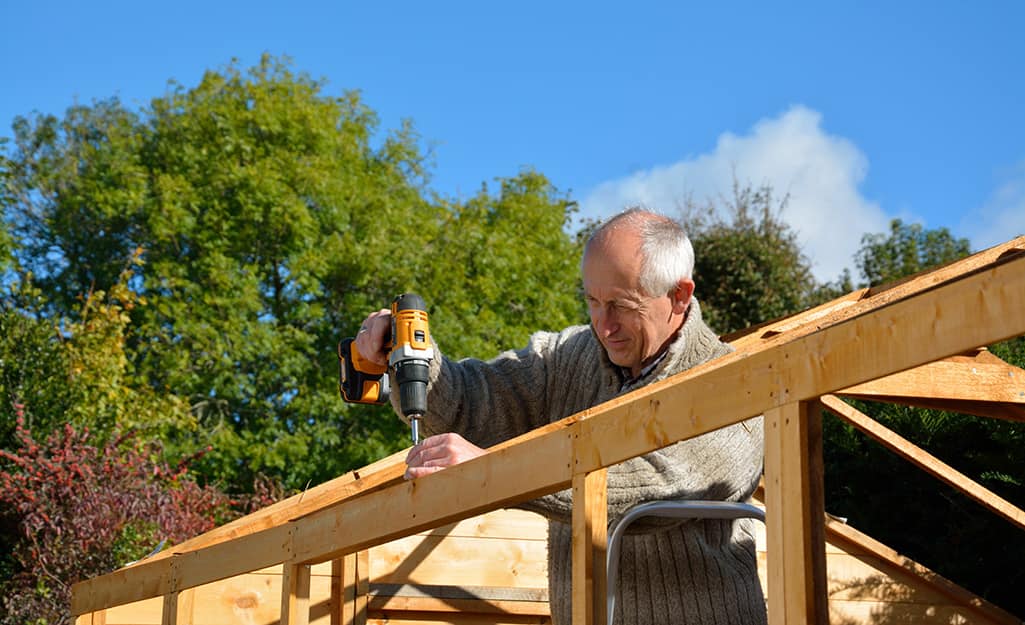 A man drilling into the post for the roof of a shed. A man drilling into the post for the roof of a shed.
