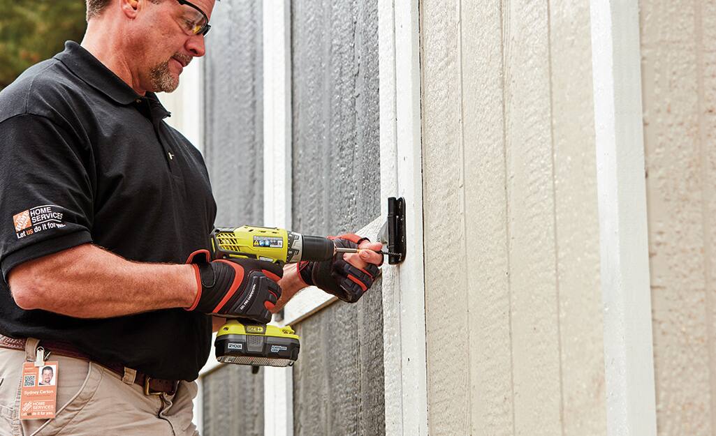A person using a drill to install the door of a shed. A person using a drill to install the door of a shed.