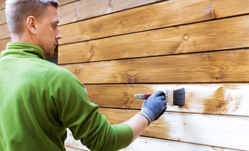 A man staining the side of a wood shed. A man staining the side of a wood shed.