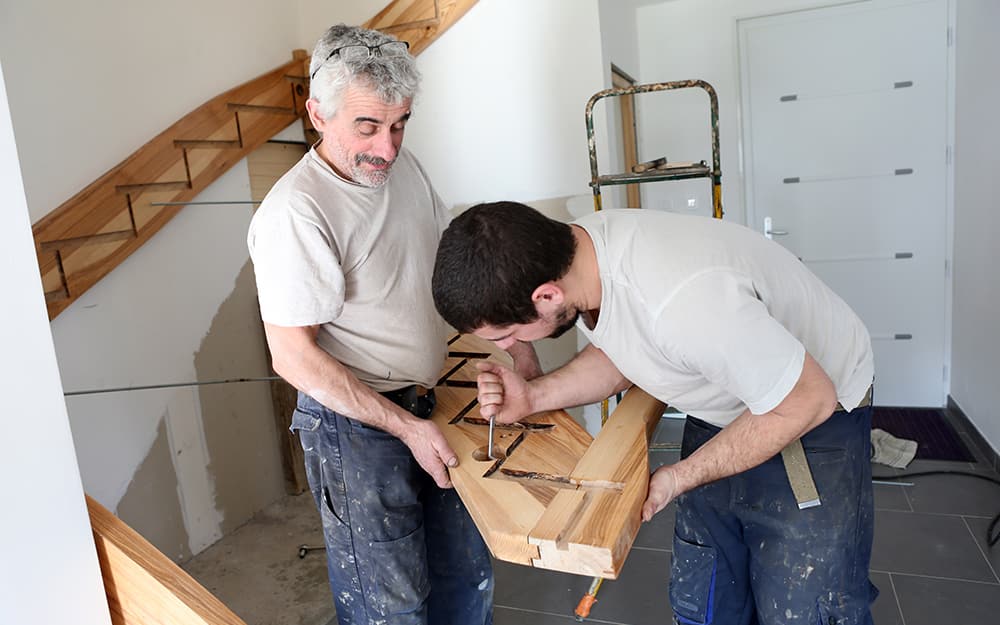 Two people carving out a hole in a staircase stringer. Two people carving out a hole in a staircase stringer.