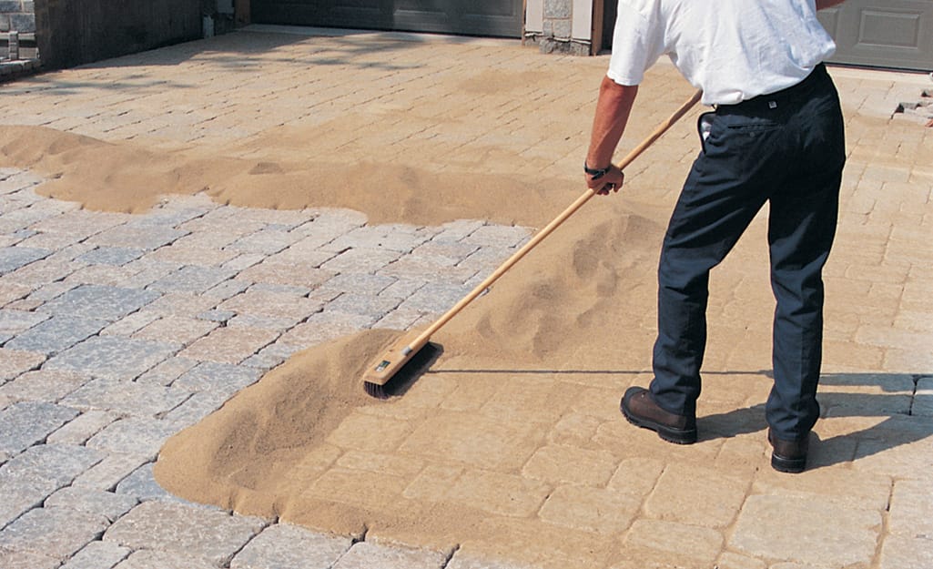 A man using a push broom to sweep sand over a paver walkway. A man using a push broom to sweep sand over a paver walkway.