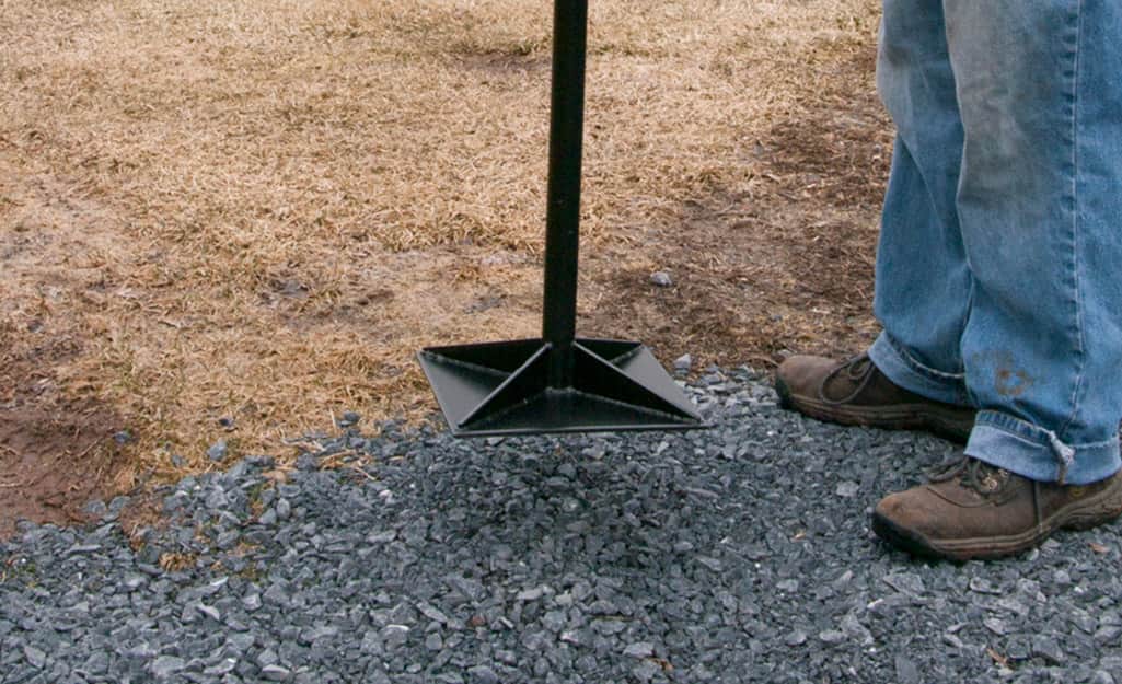 Someone using a tamp to tamp down crushed gravel for a walkway. Someone using a tamp to tamp down crushed gravel for a walkway.