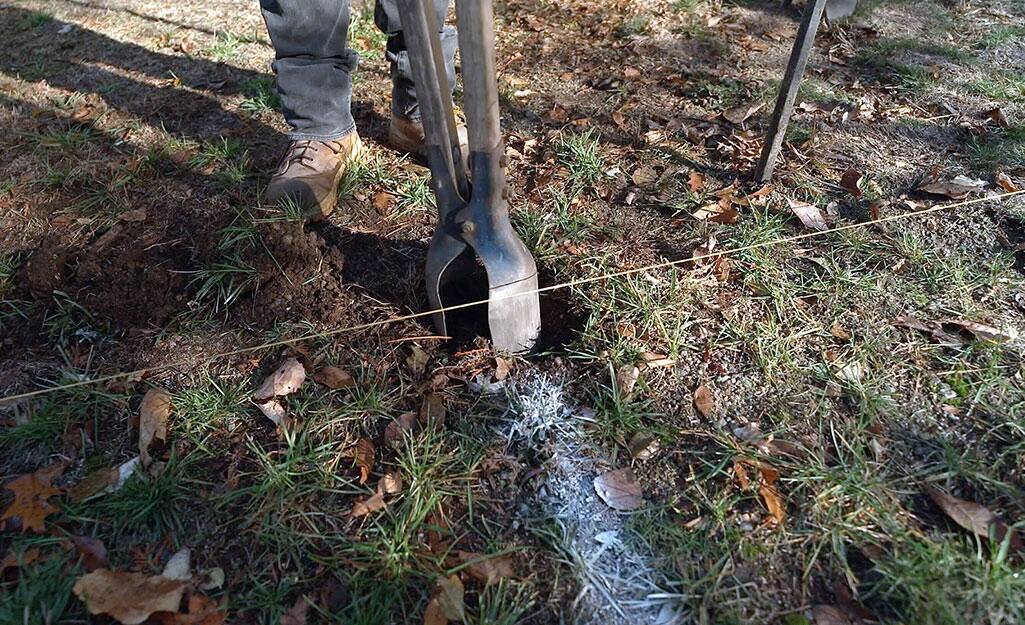 A person creating a hole with a post hole digger. A person creating a hole with a post hole digger.
