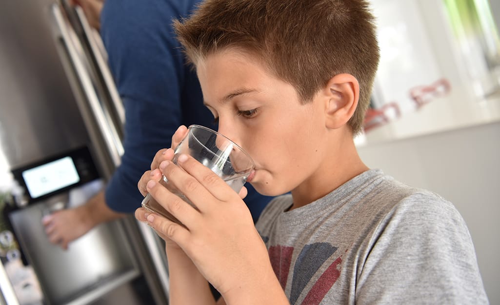A kid drinking a glass of water from the fridge. A kid drinking a glass of water from the fridge.