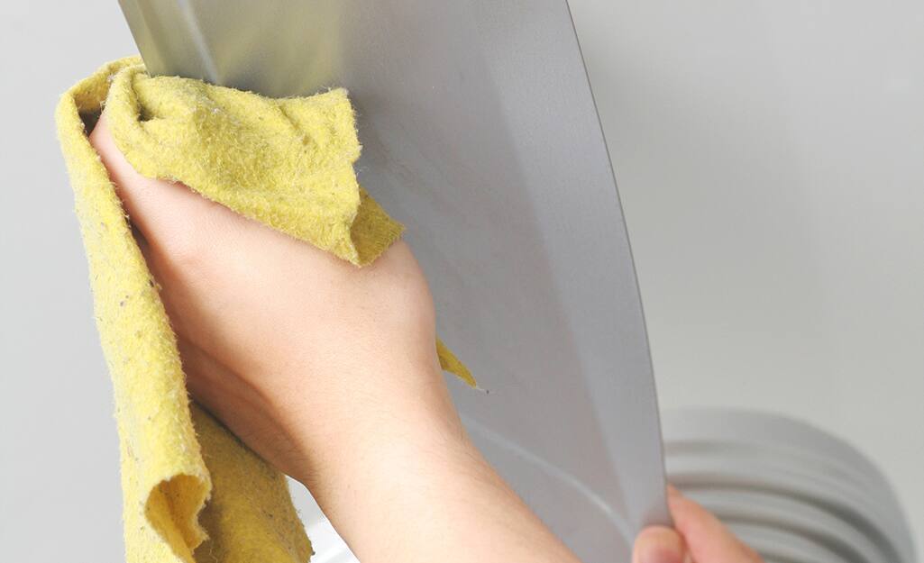 A person wiping a ceiling fan blade. A person wiping a ceiling fan blade.
