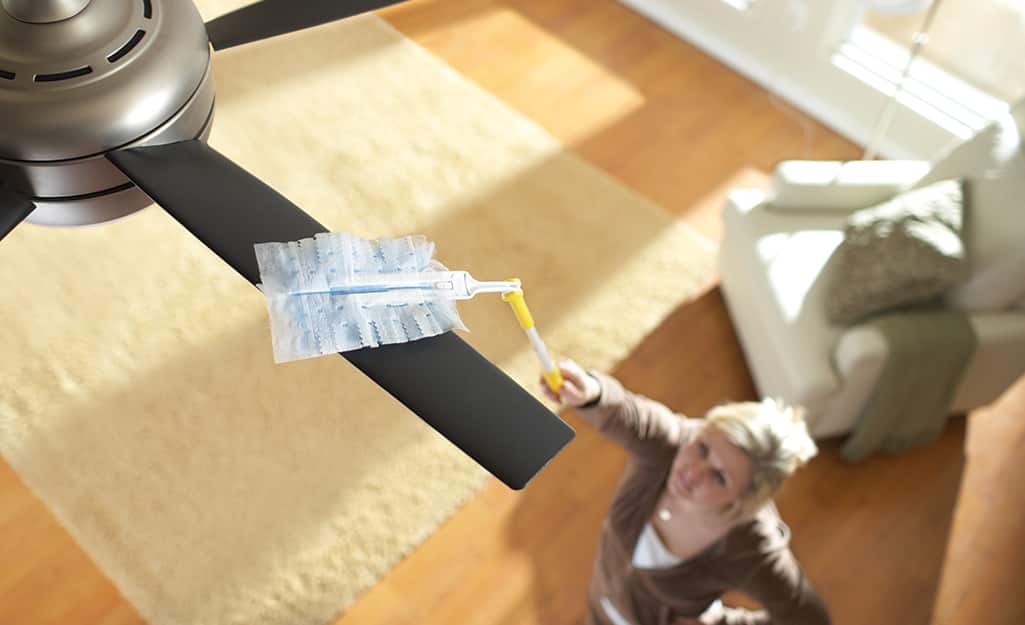 A person dusting a ceiling fan. A person dusting a ceiling fan.