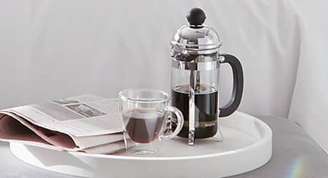 A French press coffee maker on a white tray. A French press coffee maker on a white tray.