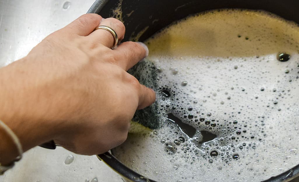 A close up of a hand scrubbing the inside of a deep fryer A close up of a hand scrubbing the inside of a deep fryer